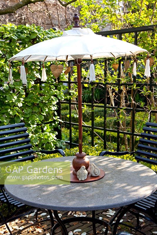 Circular garden table with small parasol and backed by black painted trellis