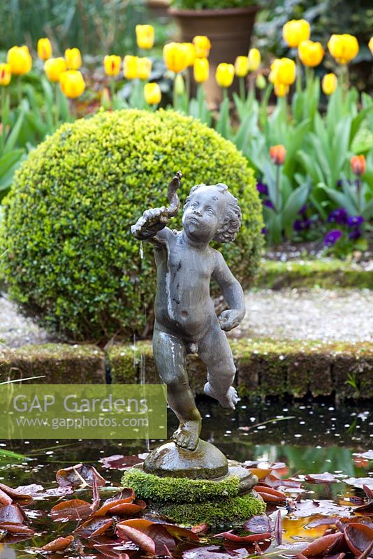 Putto statue in the centre of a circular pond with clipped Buxus ball behind