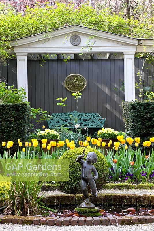 Formal garden with circular pond, beds of Tulipa 'Washington' and Tulipa 'Juliette' and clipped Buxus - Box balls 