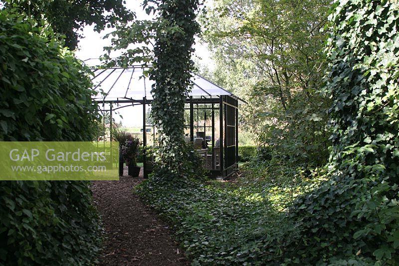 Path through woodland garden with greenhouse at the end. The Netherlands.
