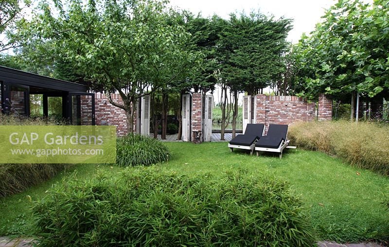 Deckchairs on lawn with trees, grasses and pruned conifers. Platanus with low growing bamboos - Hobrede, Holland