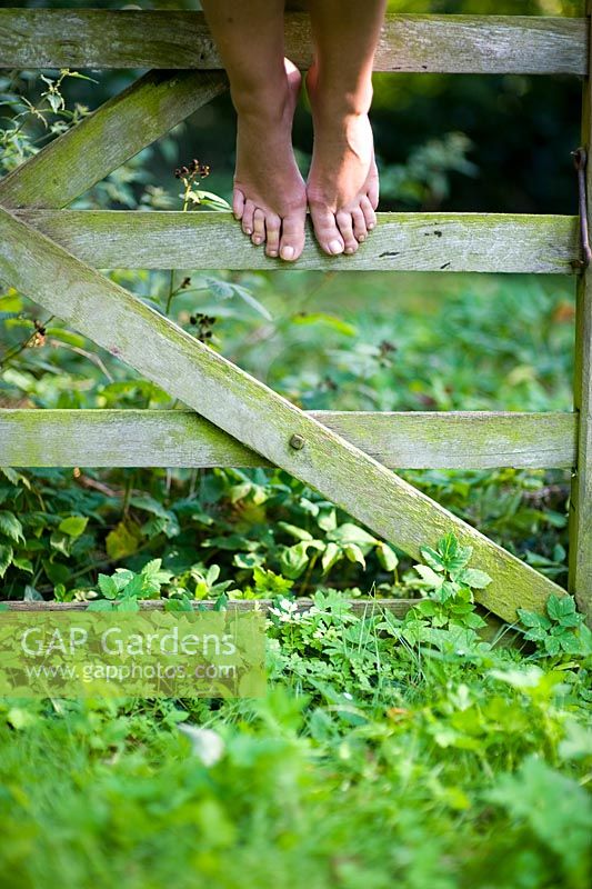 Woman with bare feet on a wooden five bar gate in summer