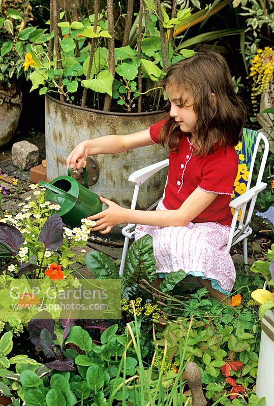 Young girl sitting in a chair, watering her own small scale kitchen garden