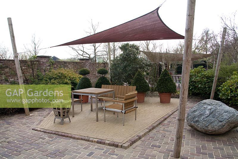 Metal and wooden furniture on patio with canvas canopy and boulder - Appeltern garden, Holland 