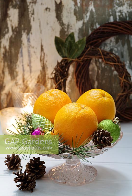Christmas baubles, fir cones and oranges on a glass dish 