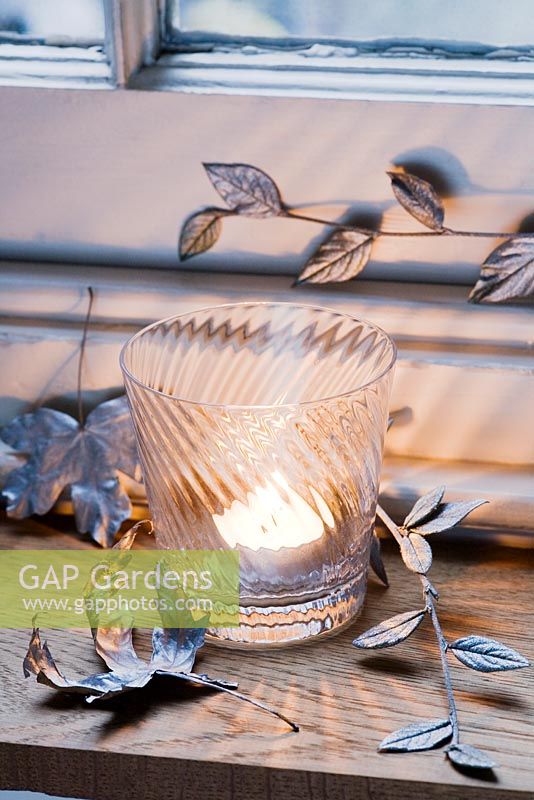 Silver sprayed leaves used as a festive decoration with a vintage glass tealight holder