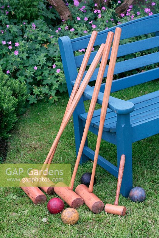 Croquet mallets leaning against a blue bench on a lawn