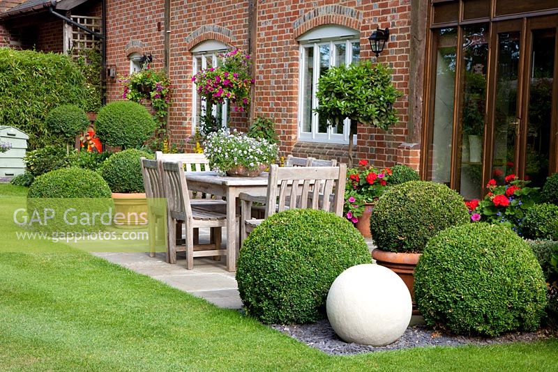 Wooden furniture on patio surrounded by Laurus nobilis and Ligustrum topiary
