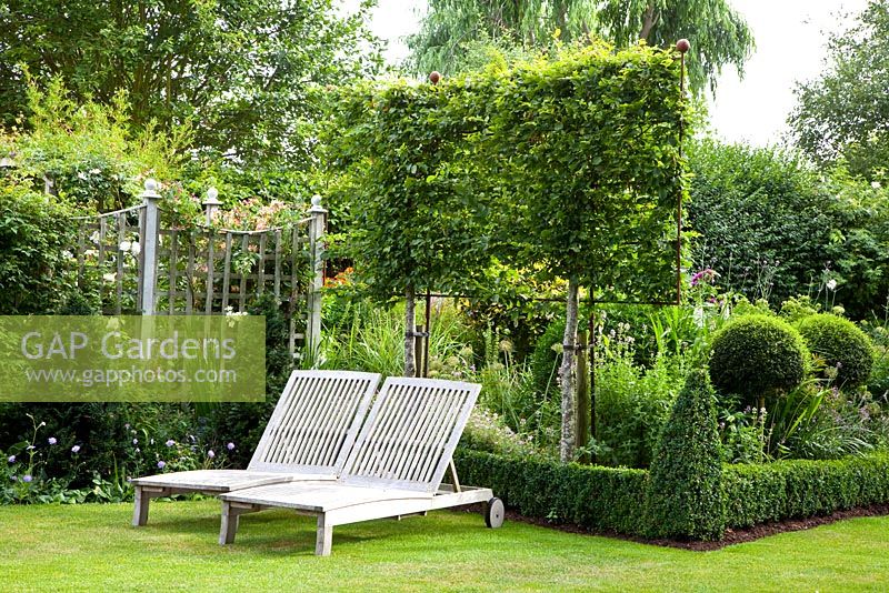 Wooden loungers on lawn, trained Carpinus betulus, clipped yew and box hedging and topiary