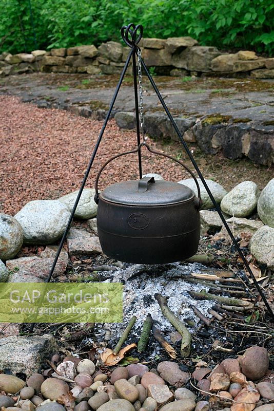 Fire pit on a gravel patio with a cooking pot and edging of boulders