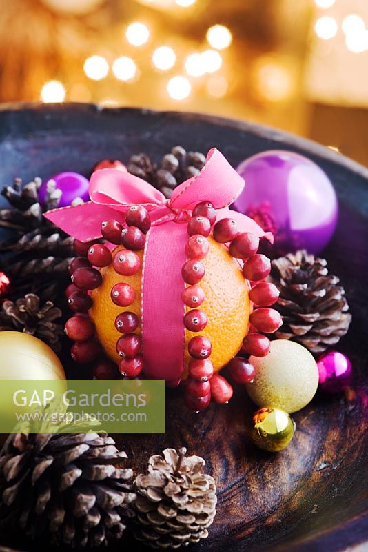 Making a Cranberry and Orange pomander for Christmas - finished pomander in a dark wood bowl with pine cones and baubles
