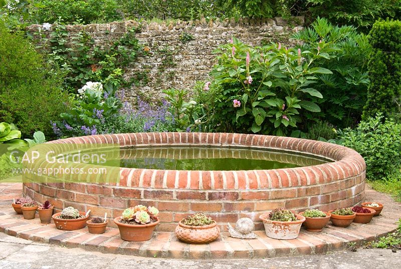 Circular brick pond surrounded by succulents in terracotta containers. Sandhill Farm House, Hampshire.