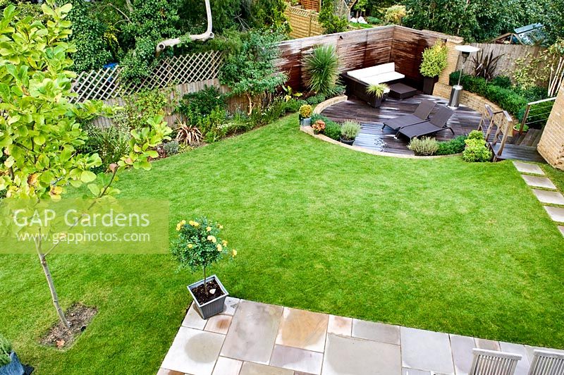 Overview of small urban garden in September with contemporary furniture and patio heater on circular sunken decked terrace. Raised bed and planting of Phormium, Arbutus unedo tree and Lavandula. Muswell Hill, London