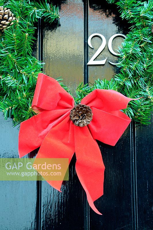 Wreath with red ribbon bow and pine cone, hanging on black door