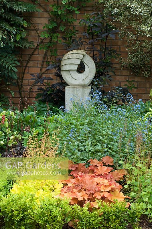 Small urban garden with stone sculpture, planting includes Heuchera, Brunnera, Sambucus nigra ,Mahonia and Euonymus - NGS garden, Foster Road, Peterborough, Cambridge