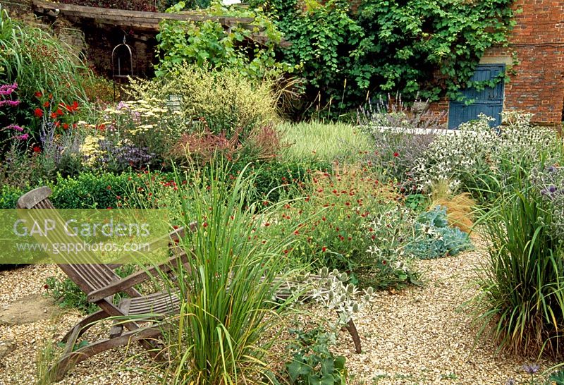 Wooden seats in gravel garden with late summer perennials and grasses.The Coach House, Hants