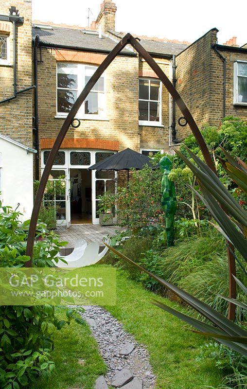Town garden with slate path over lawn and metal arch. Yulia Badian garden, London, UK 