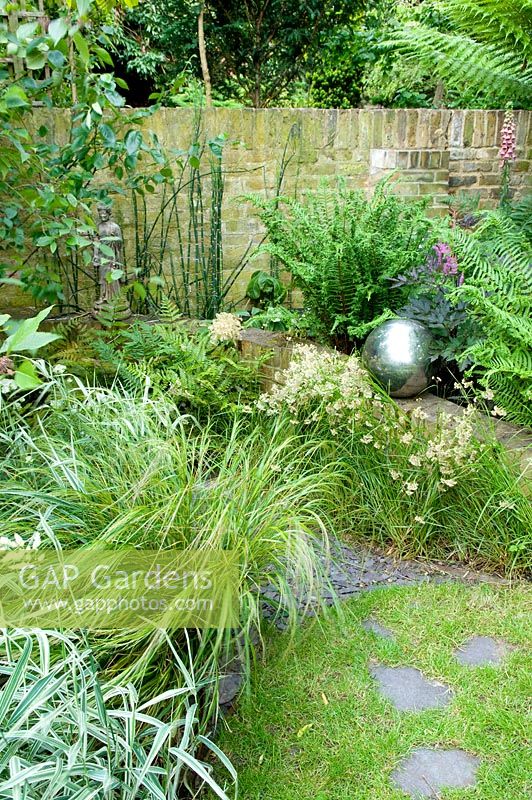 Urban garden with raised borders with Dicksonia - Tree Fern, Digitalis, Bamboos and grasses. Silver sphere focal point. Yulia Badian, London, UK