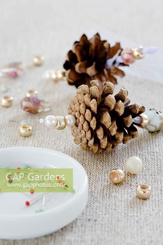 Making pine cone decorations with beads - STEP 7.  Thread 2 or 3 beads on to a pin and stick it securely in to the bottom of the pine cone