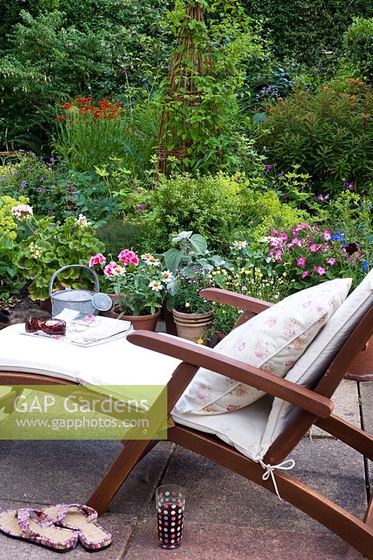 Reclining steamer chair with cushion on terrace overlooking garden border 