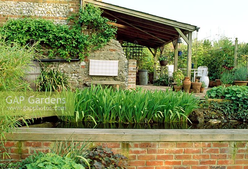 Wooden Loggia and pond with Iris foliage in late Spring. Fovant Hut Garden, Wilts