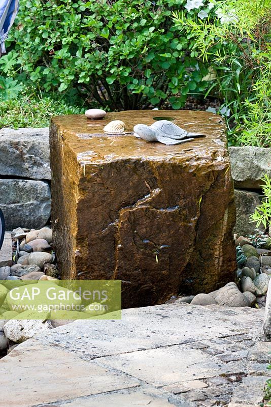 Water feature with turtoise and sea-shell on pebbles between granite paving