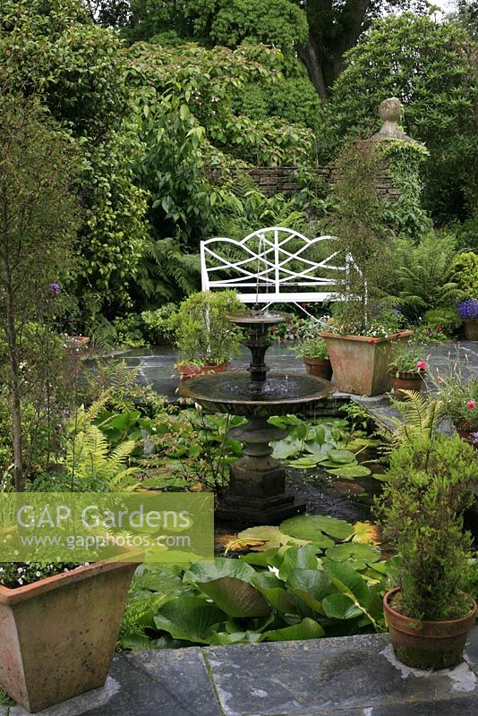 Formal garden with pool, fountain, white painted seat, containers and water lilies - The Lost Gardens of Heligan