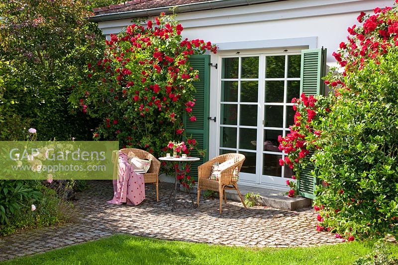 Wicker chairs and bistro table on a granite paved patio in front of a window with climbing roses