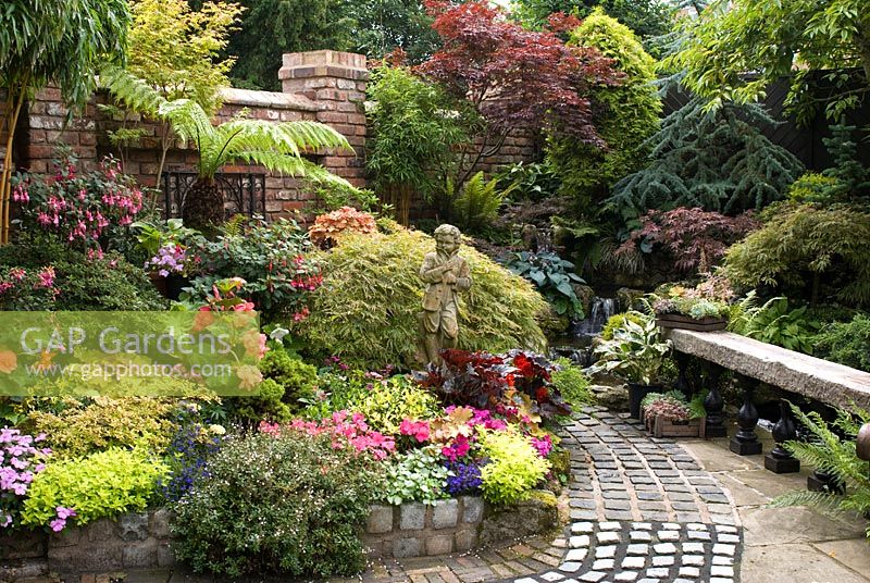 Cobble path leading to waterfall, bench made from reclaimed railway sleeper and mixed rich late summer borders including Fushia, Begonia, Impatiens, Dicksonia antartica, Acer, Hosta, conifers and ferns - Brocklebank Road, Southport, Lancashire NGS
 