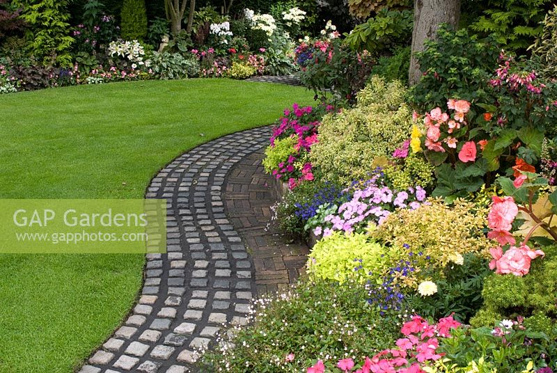 Reclaimed cobbles and bricks used to make curving path by lawn and raised border with mixed rich late summer planting including Parahebe, Pieris, Begonia, Impatiens and Lobelia. Brocklebank Road, Southport, Lancashire NGS