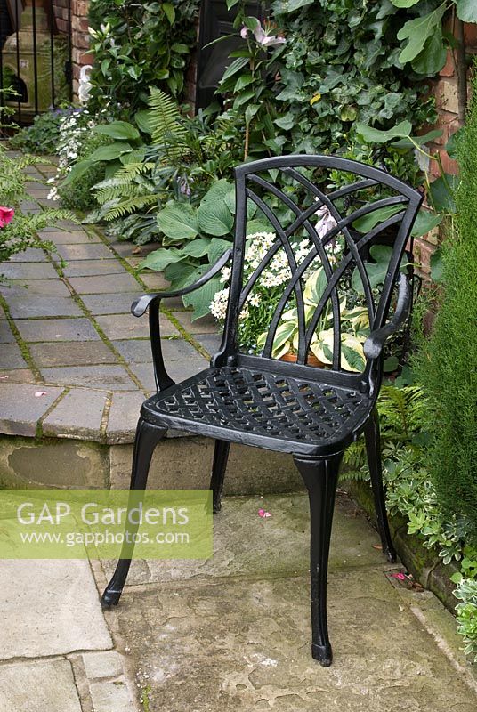 Cast iron decorative chair on stone slab patio, Hosta and Hedera behind - Brocklebank Road, Southport, Lancashire NGS