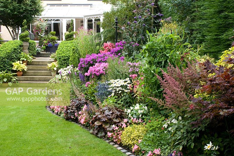 Late summer border with Buddleia, Acer, Euonymus, Phlox 'Nicky', Phlox paniculata 'Pink Flame', Eryngium, Leucanthemum, Liatris spicata, Heuchera 'Purple Palace', Begonia 'Ambassador Pink' and Veronica spicata 'Royal Candles' leading to steps with Hosta pots and patio - Brocklebank Road, Southport, Lancashire NGS 
