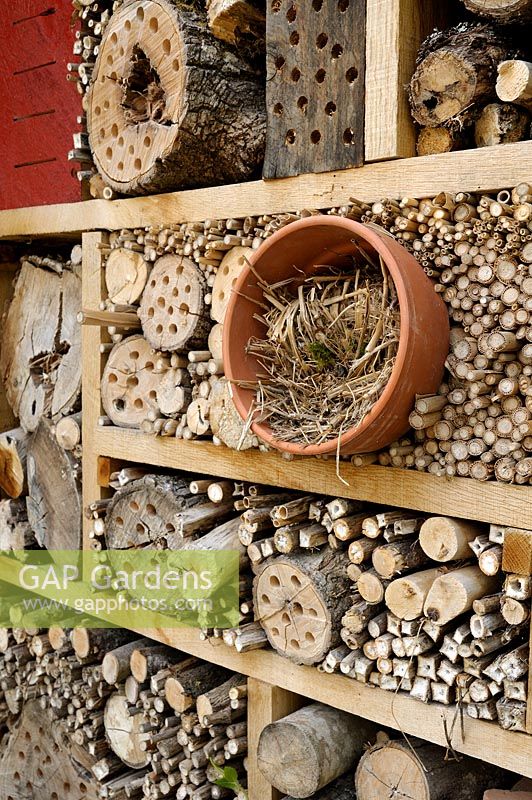 Insect house made from logs, bamboos and straw in clay pot