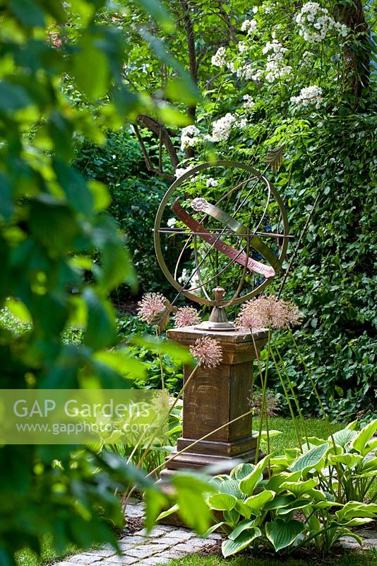 Sundial on a stone pillar backed by a hedge with Rosa 'Rambling Rector', flowerbed of Hosta fortunei 'Aureomarginata' and Allium giganteum - The Manor House, Germany