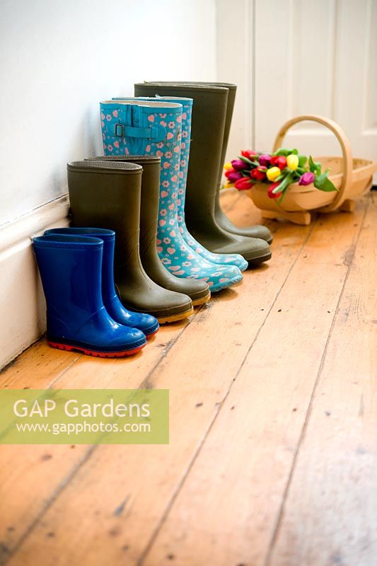 Four pairs of wellies of a gardening family in hallway with a wooden trug of Tulips