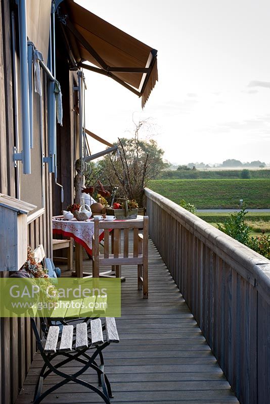 A narrow balcony with wooden and iron chairs and dressed table and chairs with views of the dike of the Elbe, Germany