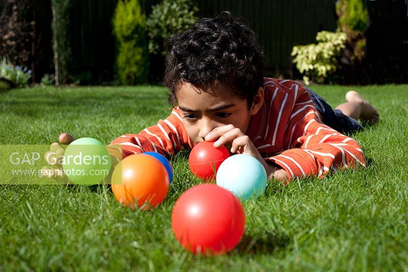 Boy lying down on grass playing with brightly coloured balls
