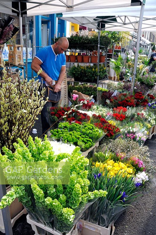 Colourful display of flowers on stall with stallholder Columbia Road Flower Market, Tower Hamlets London UK