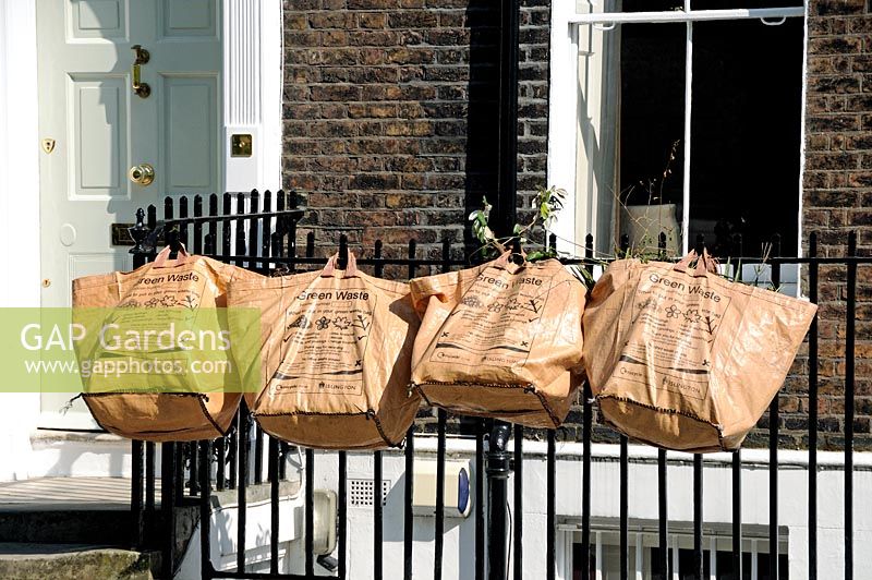 Green waste bags hanging on railings awaiting collection, Highbury London UK
