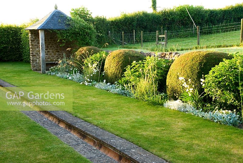 Rill garden with pair of gazebos and borders containing clipped Lonicera nitida, Helictotrichon sempervirens, Rosa rugosa 'Alba' and silvery Stachys lanata, enclosed at one end by hornbeam hedge. Private garden, Dorset, UK