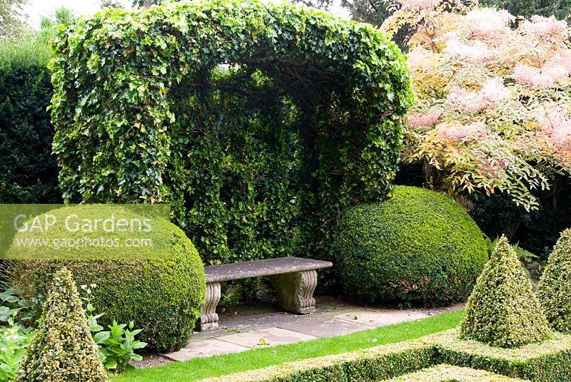 Hedera - Ivy covered port-cullis shaped gazebo at the end of the Knot Garden of clipped Buxus - Box. Bourton House, Bourton-on-the-Hill, Moreton-in-Marsh, Glos, UK
