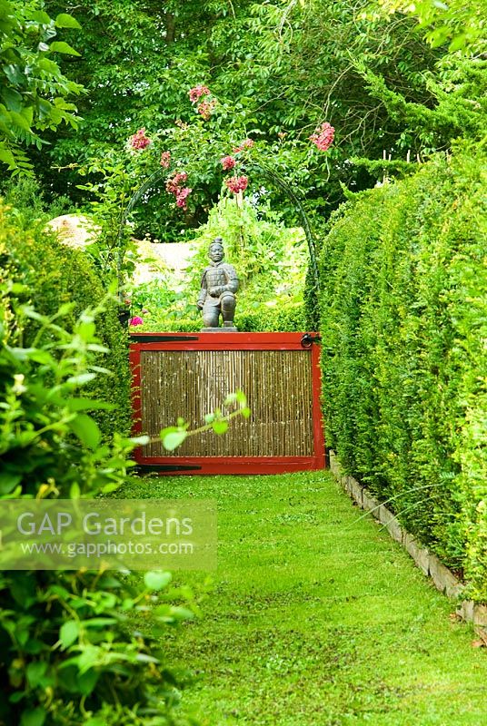 View along axis to statue of a terracotta warrior from Xi'an crouching on a pedestal marked with the word 'China', seen through bamboo gate below Rose arch. Beggars Knoll, Newtown, Westbury, Wiltshire, UK