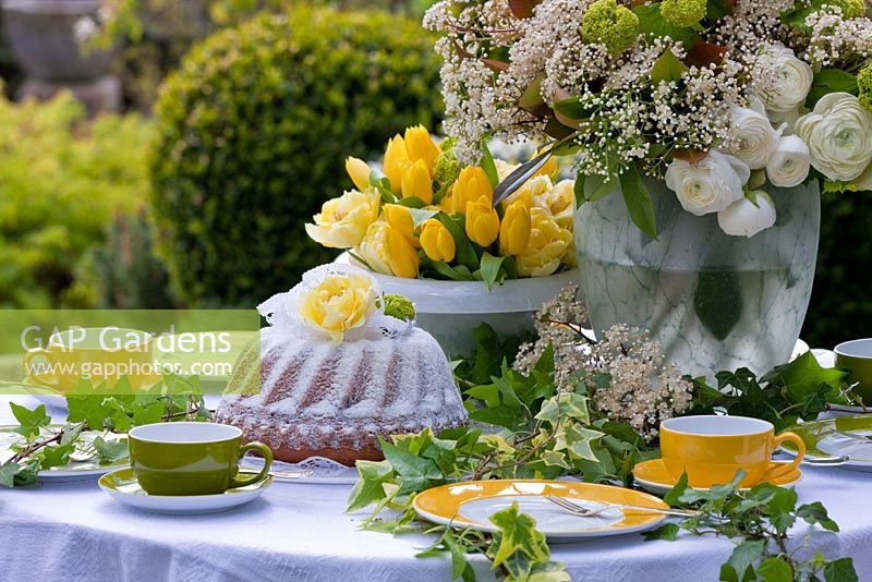 An inviting decorated table with green and yellow dishes, a bundt cake, Tulips, Ranunculus and a white bouquet - Wintergarten, Germany
 