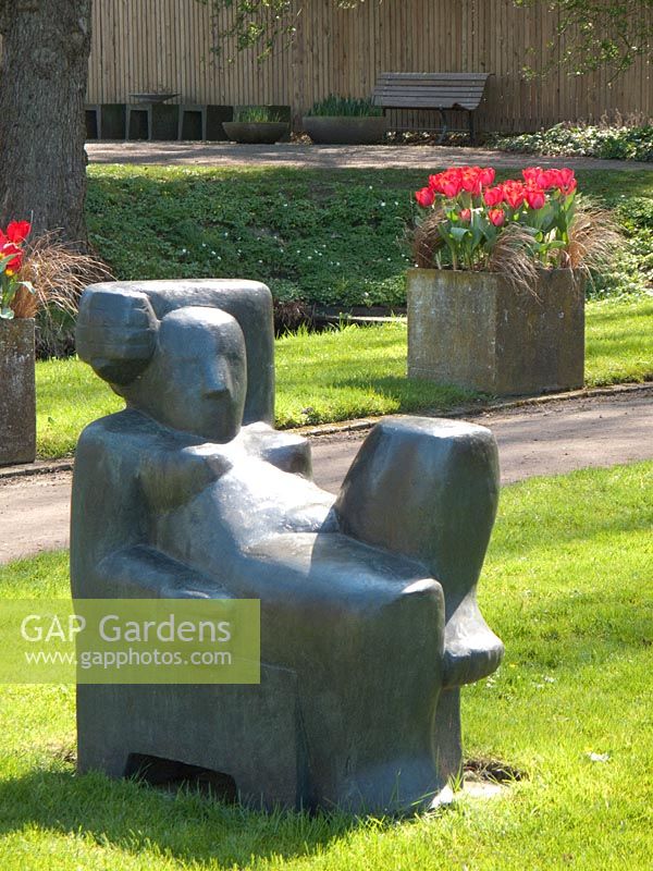 Modernist sculpture lounging on lawn. Tulipa 'Red Flair' planted with Carex Bronze Form in a square stone containers. Mien Ruys Tuinen, Dedemsvaart, Netherlands 