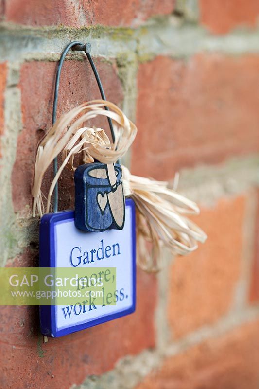 'Garden more, work less' sign hanging on a brick wall