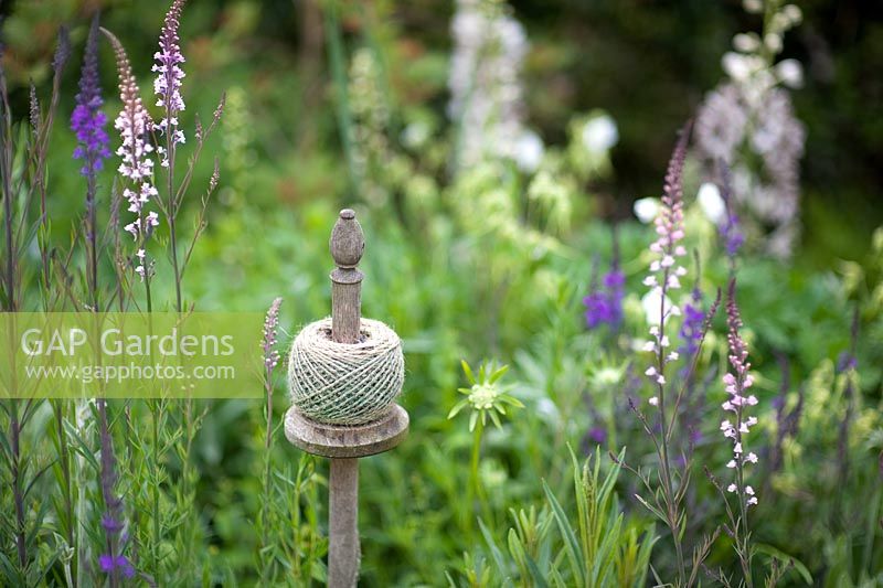 Ball of string on a wooden post surrounded by cottage planting of Linaria Purpurea 'Canon Went' and Delphinium 'Sandpiper'.  Lychnis coronaria and Stachys lanata in the front.