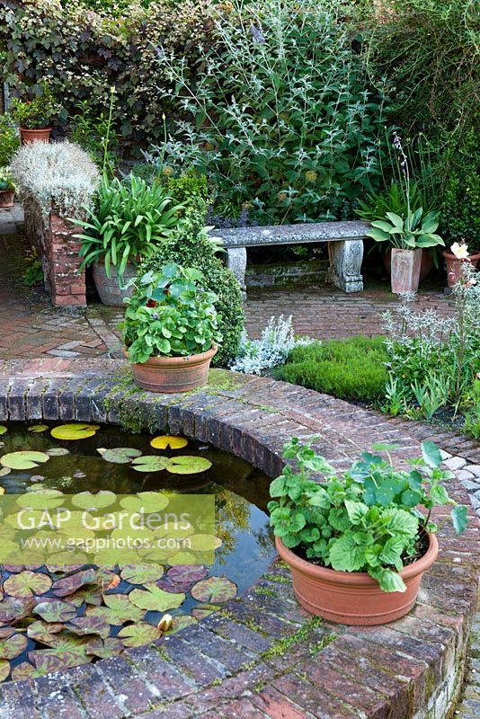The Corner House, Wiltshire. Summer garden, small brick circular pond with lily pads