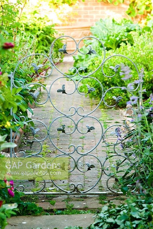 Decorative metal gates are a feature throughout the garden, here connecting the walled kitchen garden with the patio outside the kitchen - Old Rectory, Kingston, Isle of Wight, Hants, UK