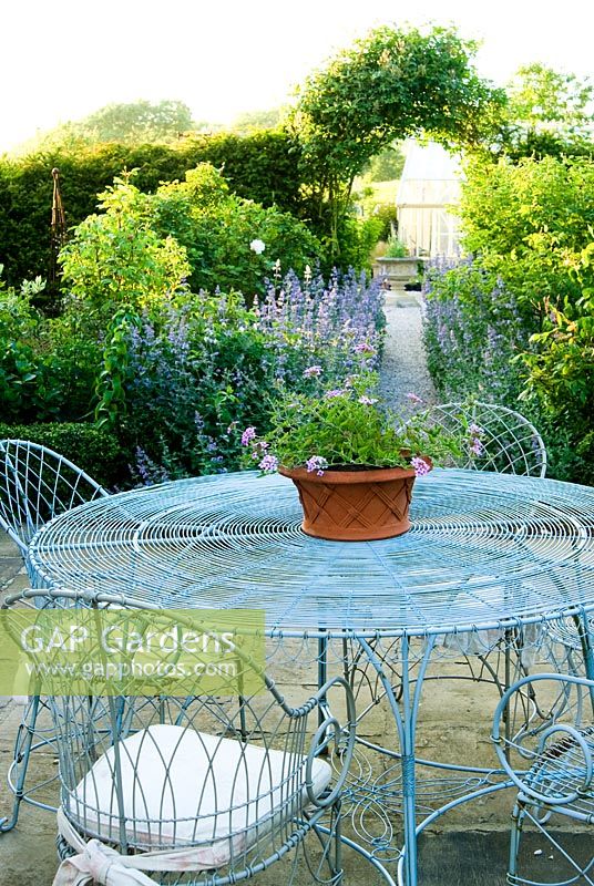 Decorative wirework chairs and table on the terrace outside the kitchen, with Nepeta 'Six Hills Giant' - Catmint, lining the path leading further into the garden - Old Rectory, Kingston, Isle of Wight, Hants, UK