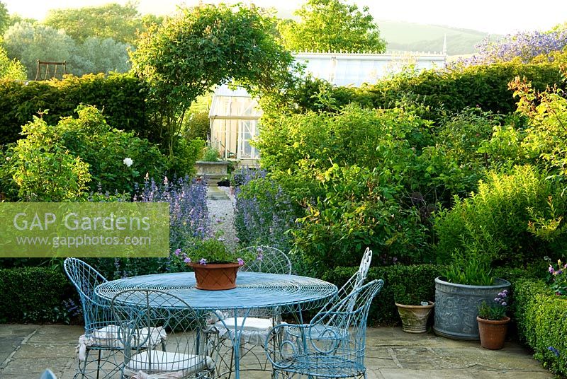 Decorative wirework chairs and table on the terrace outside the kitchen, with Nepeta 'Six Hills Giant' - Catmint, lining the path leading into the garden.  Old Rectory, Kingston, Isle of Wight, Hants, UK